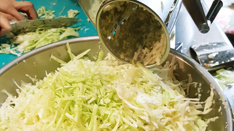 Cabbage being shredded by a kitchen aid attachment.
