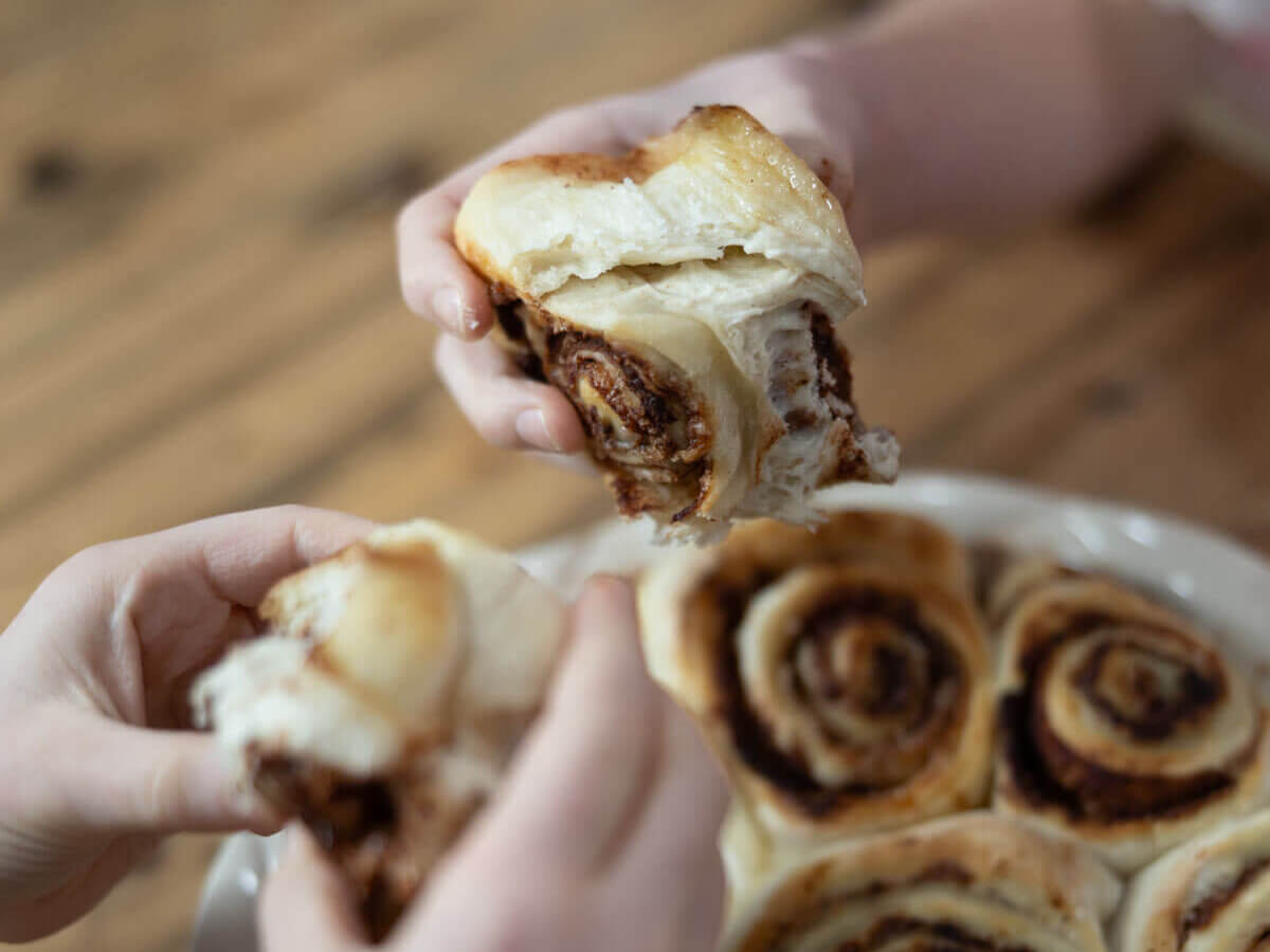 Hands pulling gluten free cinnamon rolls from a pan.