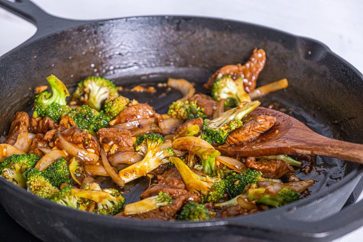 Beef and broccoli stir frying in a cast iron pan.