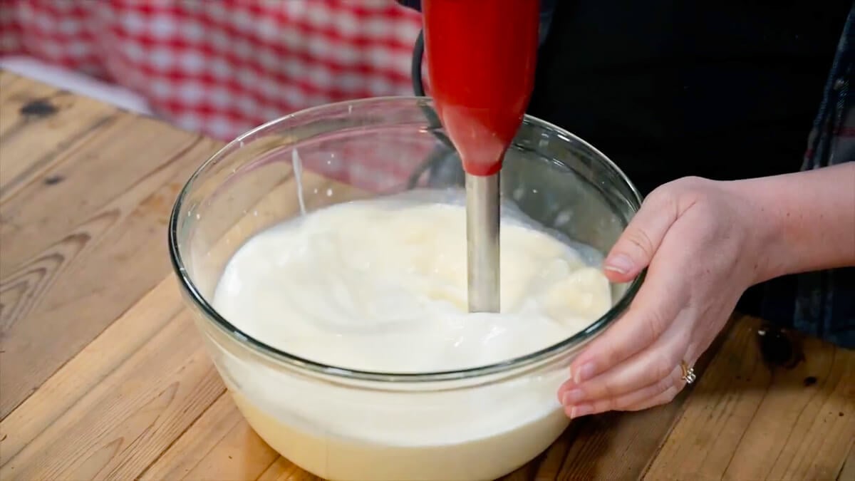 An immersion blender mixing homemade eggnog ingredients together in a bowl.