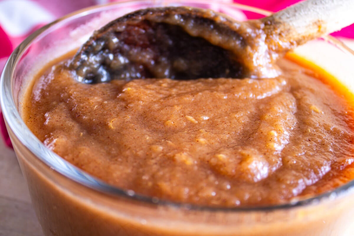 A wooden spoon stirring applesauce in a bowl.