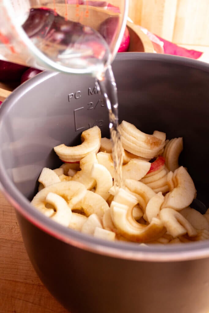 Water pouring into an Instant Pot insert full of peeled and sliced apples.