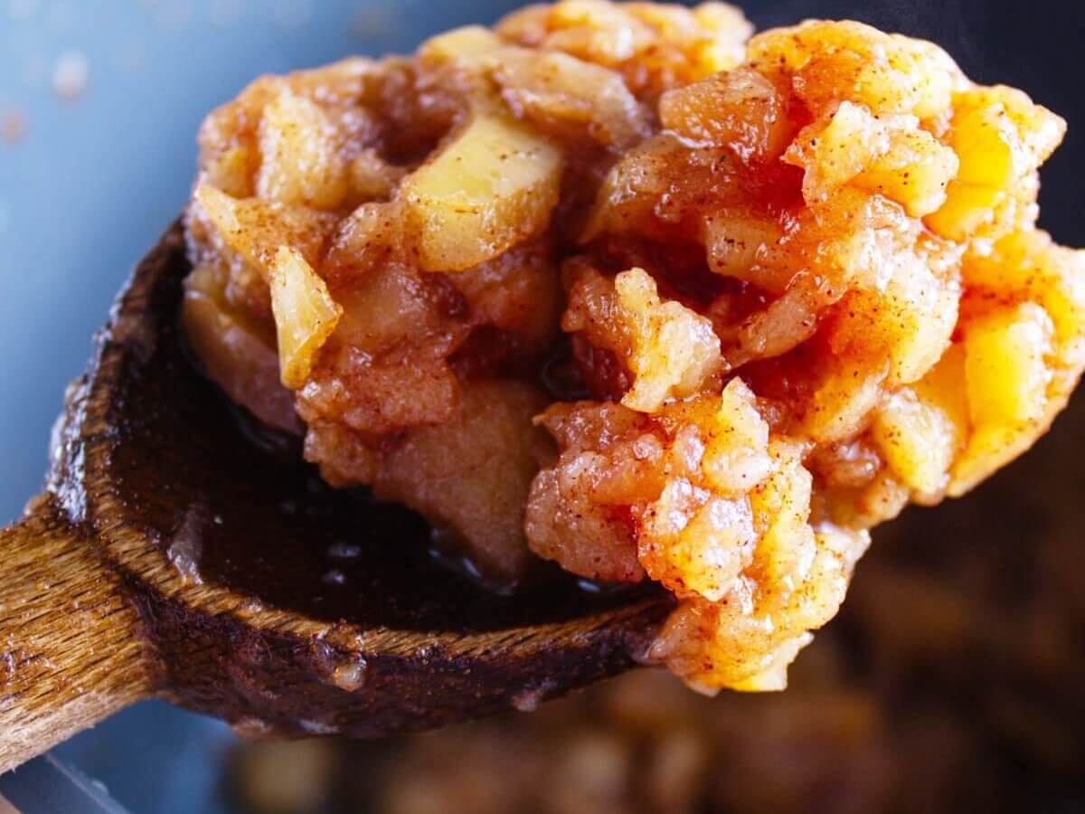 A spoon lifting cooked apples out of an Instant Pot ready to pureé into applesauce.