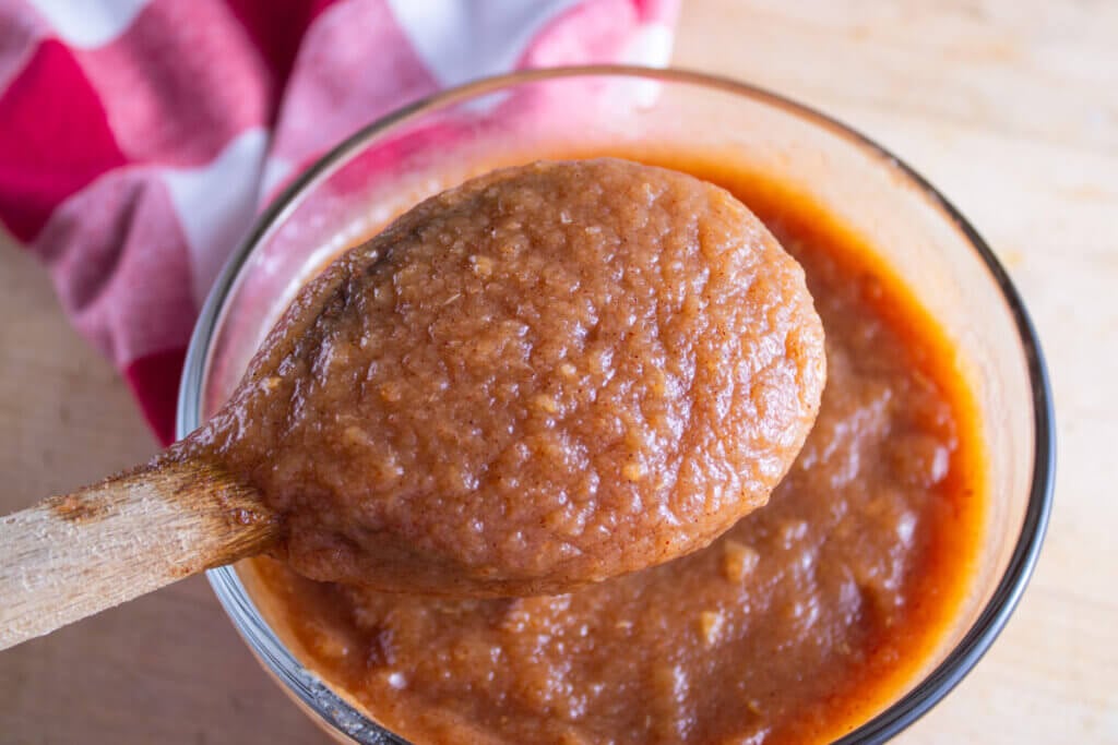 A wooden spoon lifting a serving of applesauce from a bowl.
