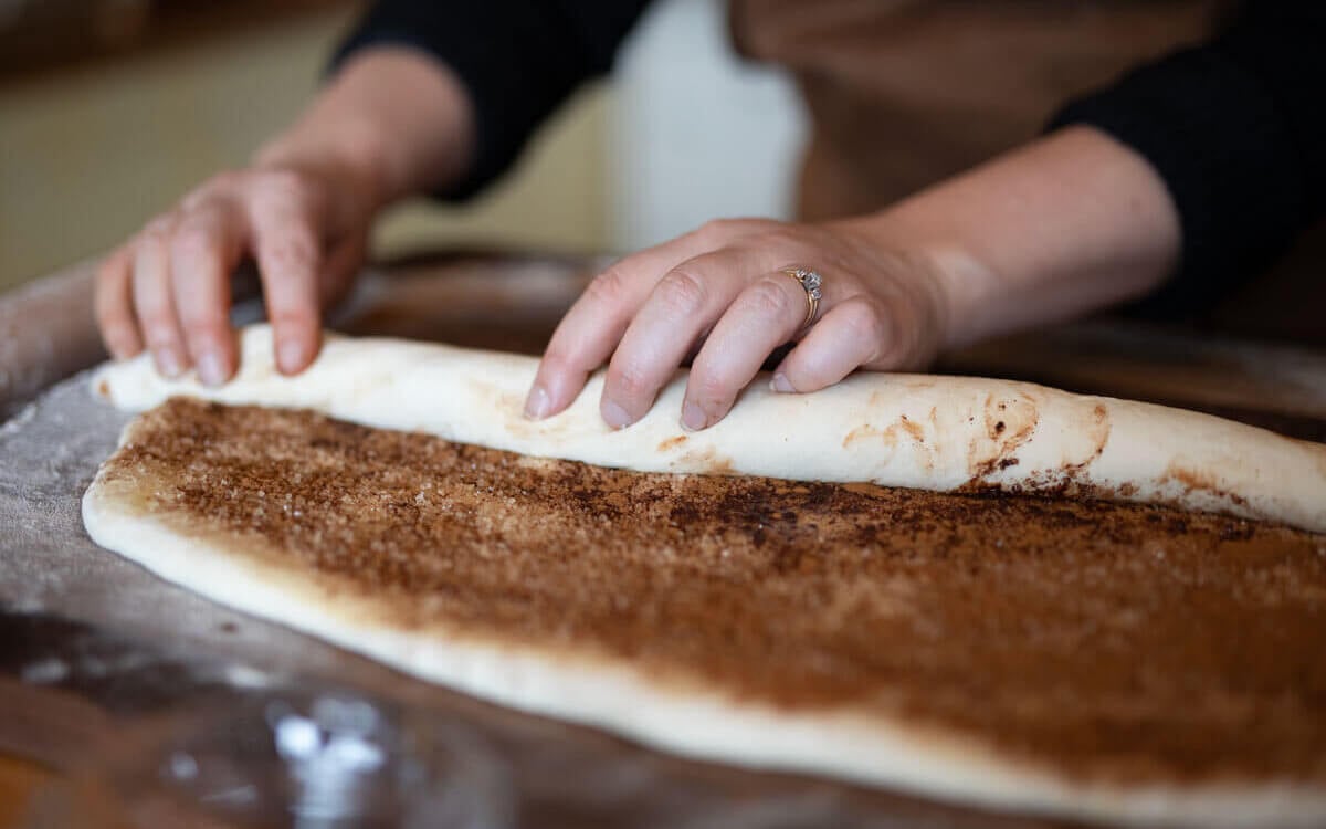 Hands rolling cinnamon roll dough.