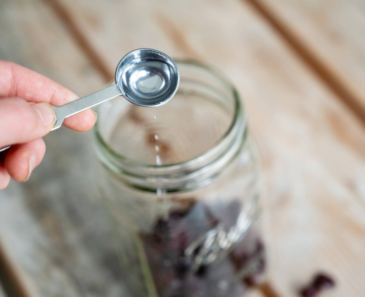 Adding almond extract to a glass jar with dried cherries in the bottom.