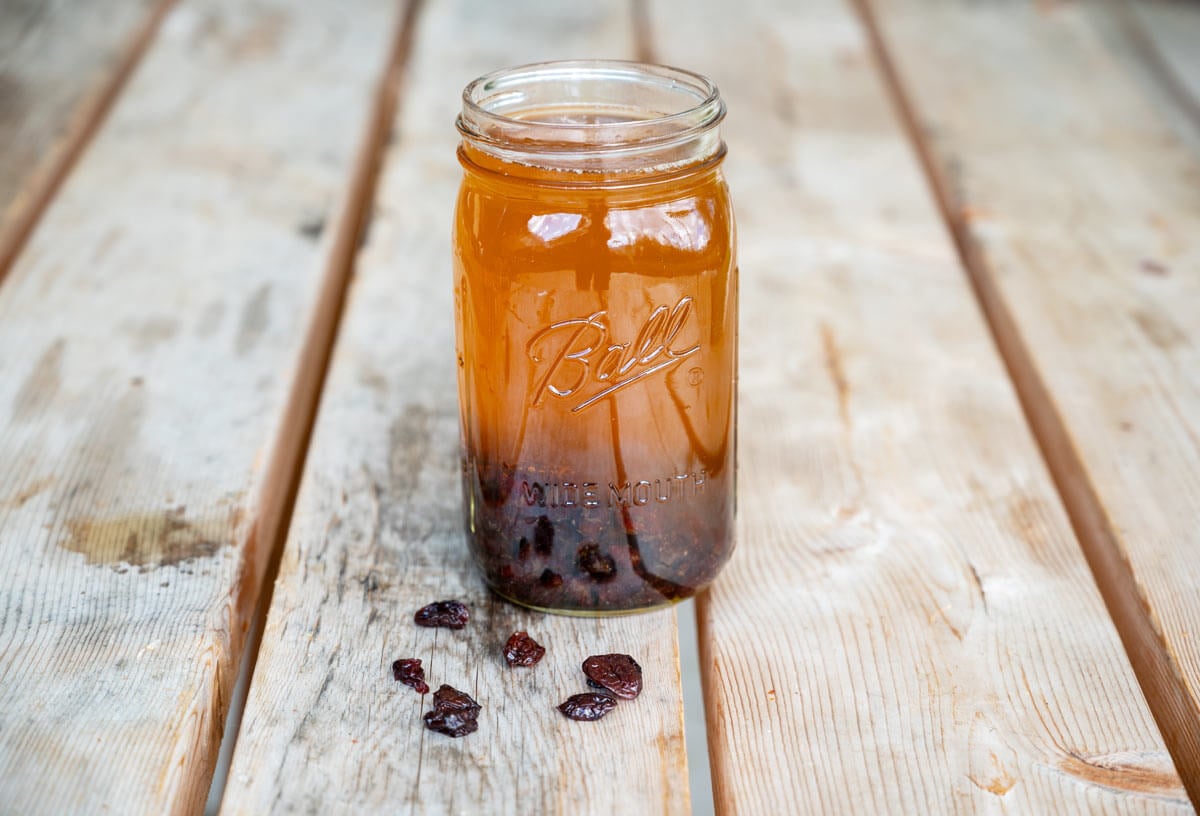 A glass jar full of kombucha with dried cherries in the bottom.