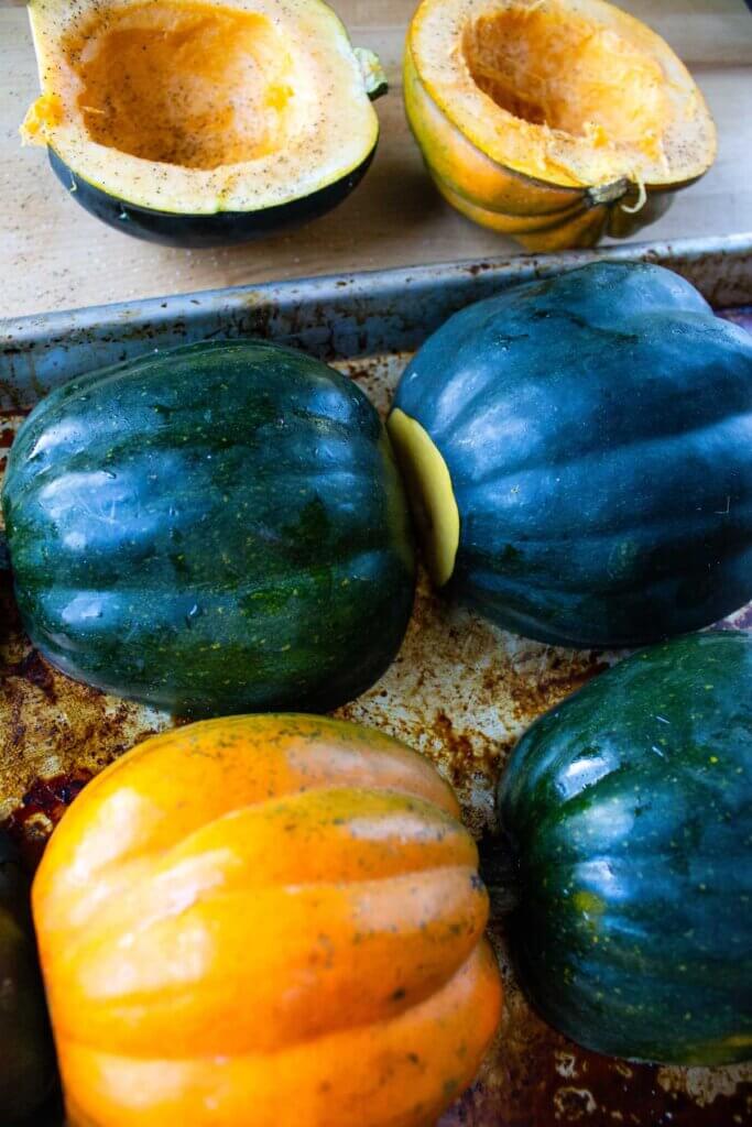 Acorn squash sliced in half and placed face down on a baking sheet.