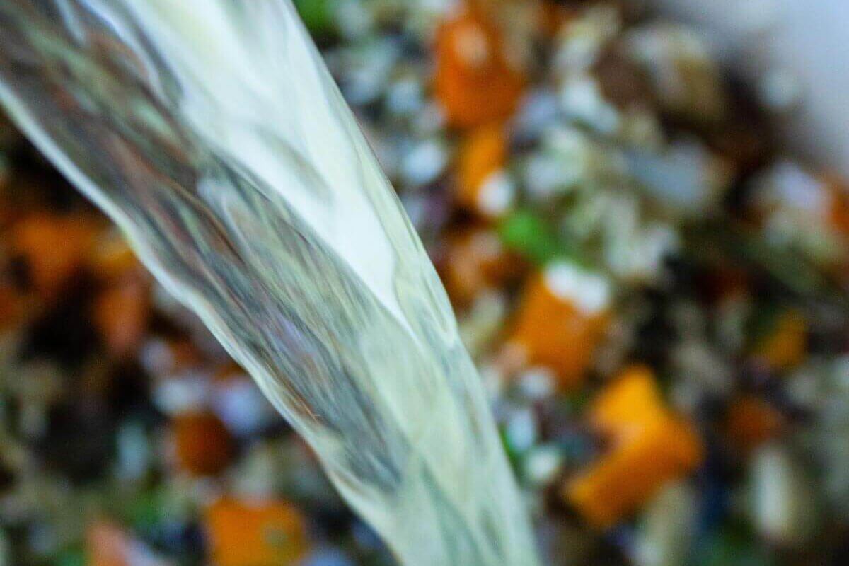 Chicken broth pouring into a Dutch oven filled with wild rice, carrots, onions, celery, and mushrooms.
