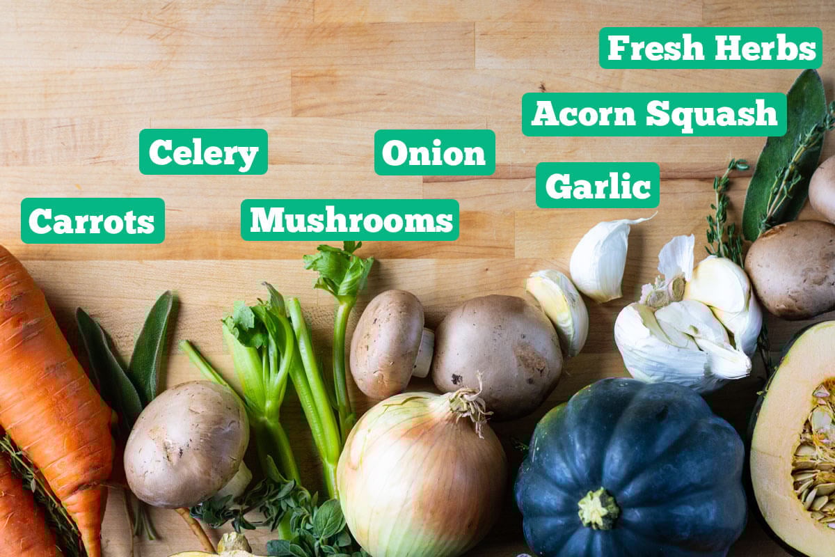 Stuffed acorn squash ingredients: celery, mushrooms, onion, carrots, acorn squash, garlic, and fresh herbs.