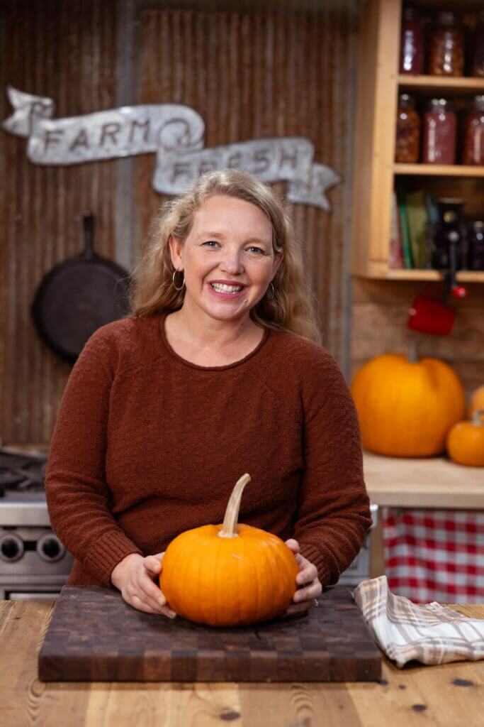 A woman in the kitchen with a pumpkin.
