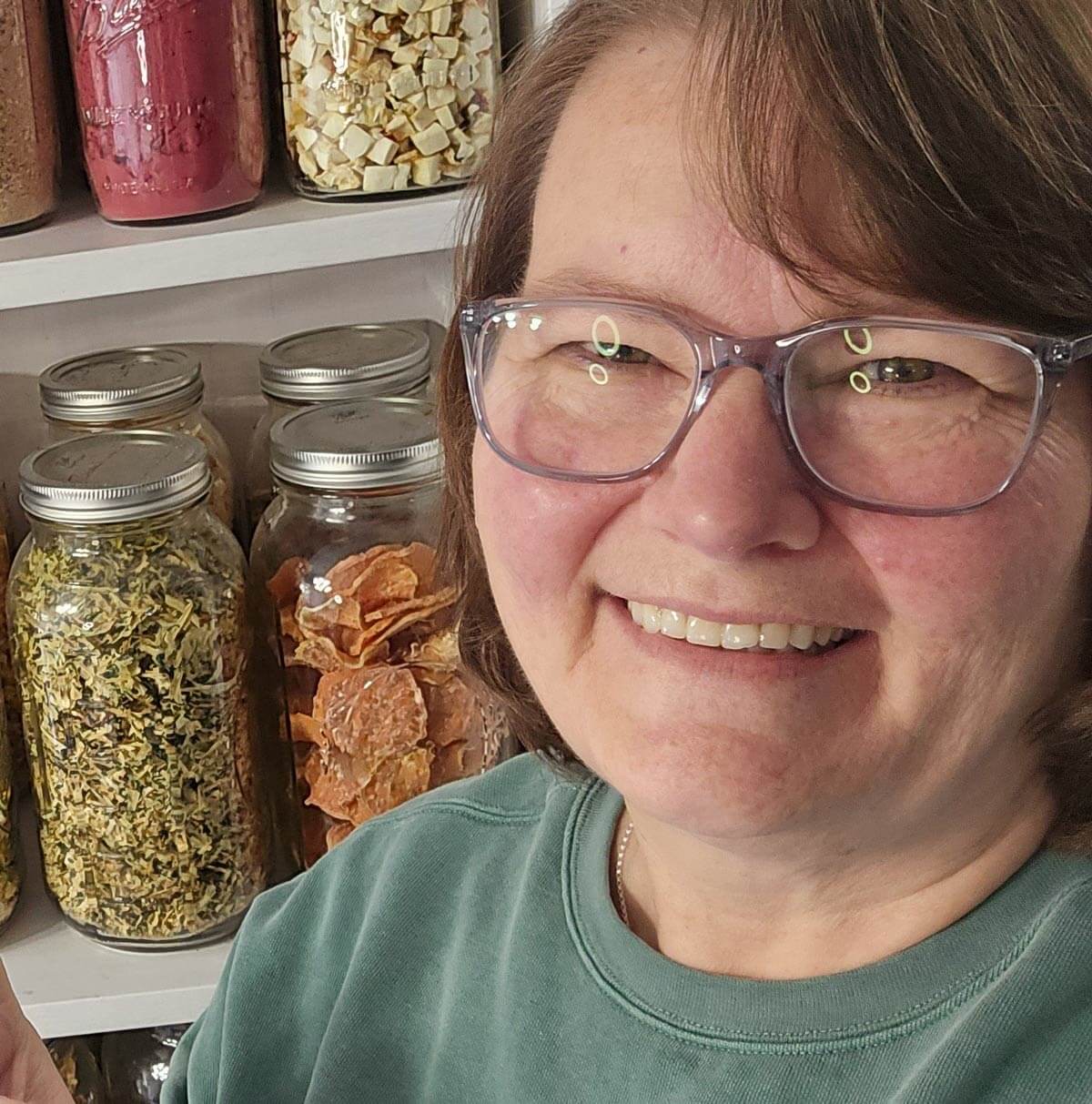 A woman standing in front of a pantry lined with jars of dehydrated food.