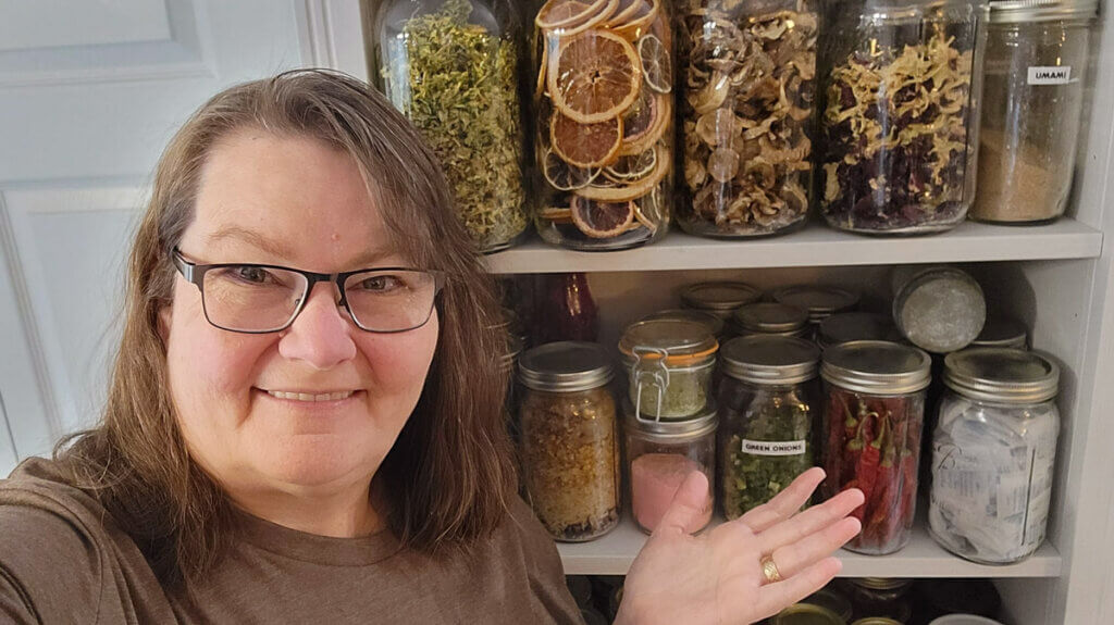 A woman standing in front of a pantry lined with jars of dehydrated food.