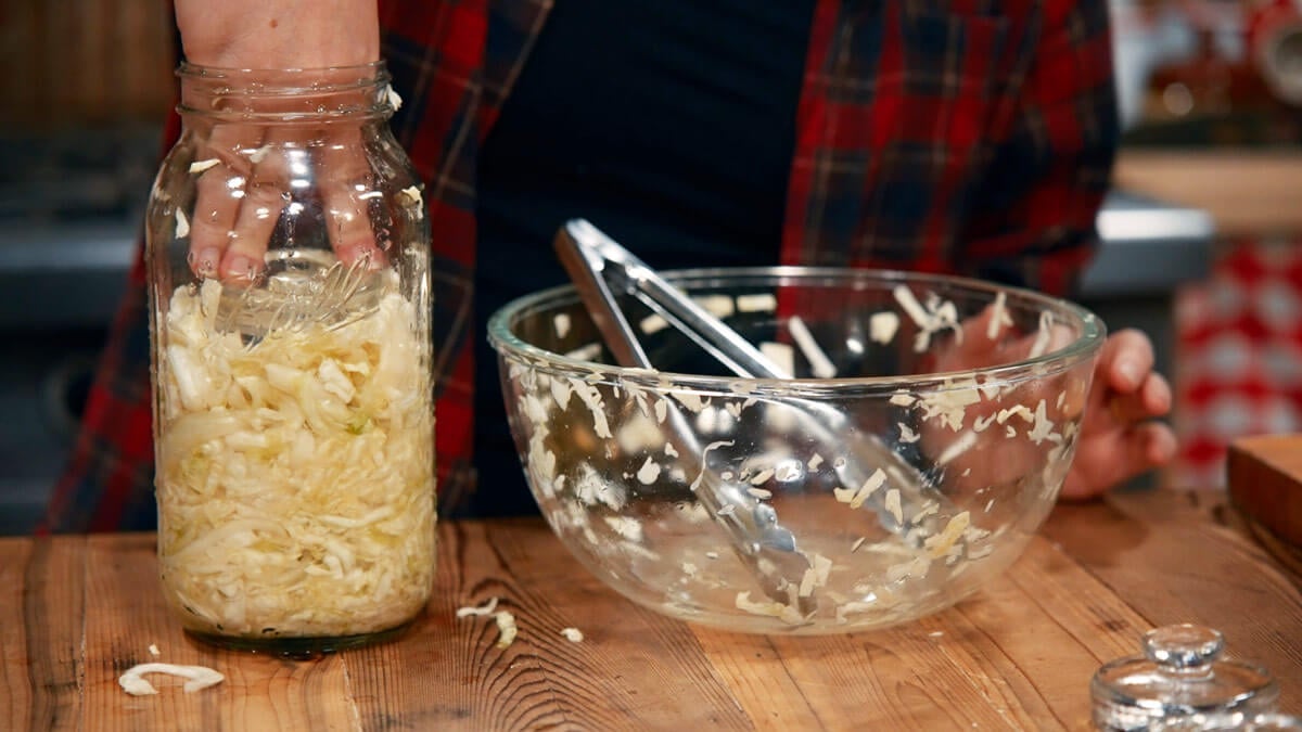 A fermentation weight being added to a jar of sauerkraut.