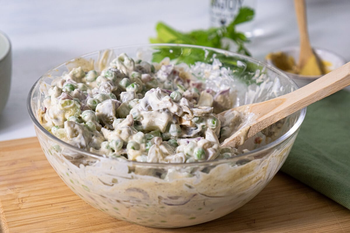 Green pea salad mixed with dressing in a large bowl.