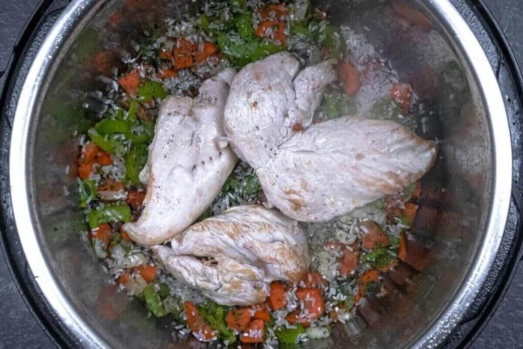 Cooked chicken breast in an Instant Pot being cooked with vegetables.
