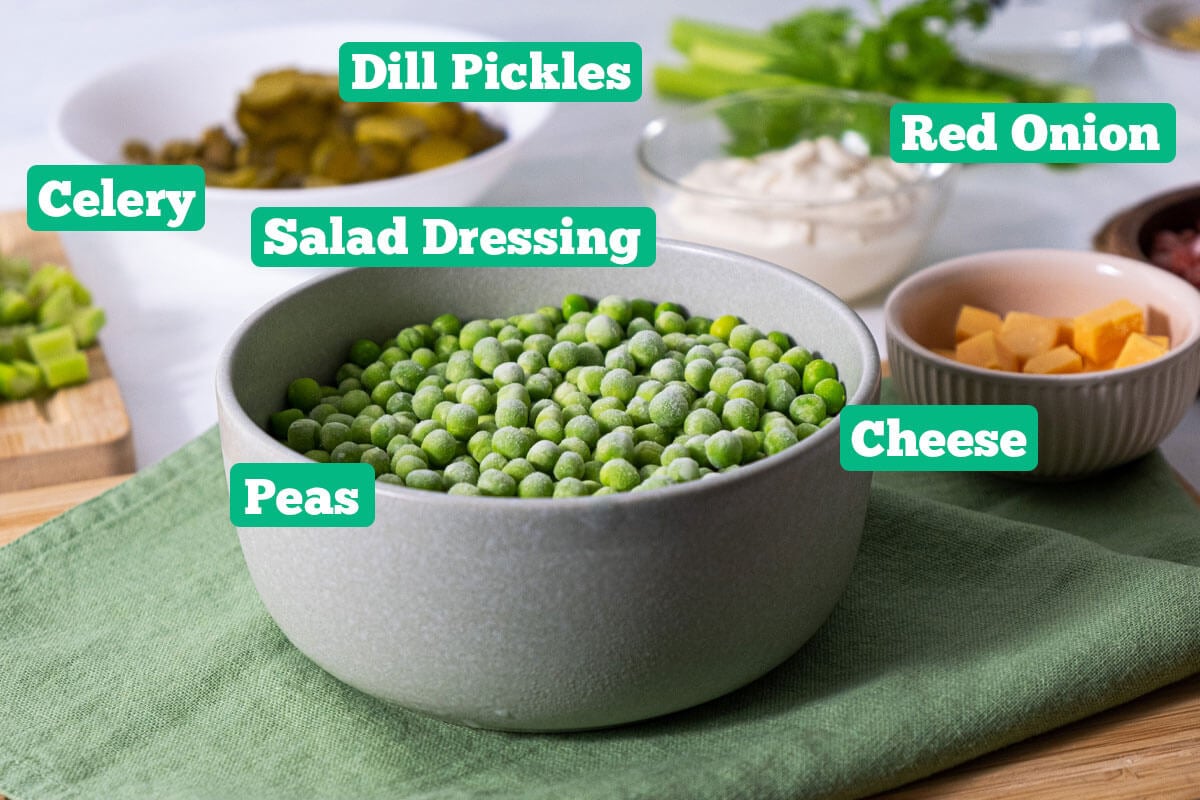 Frozen green pea salad ingredients: dill pickles, salad dressing, red onion, cheese, and peas.