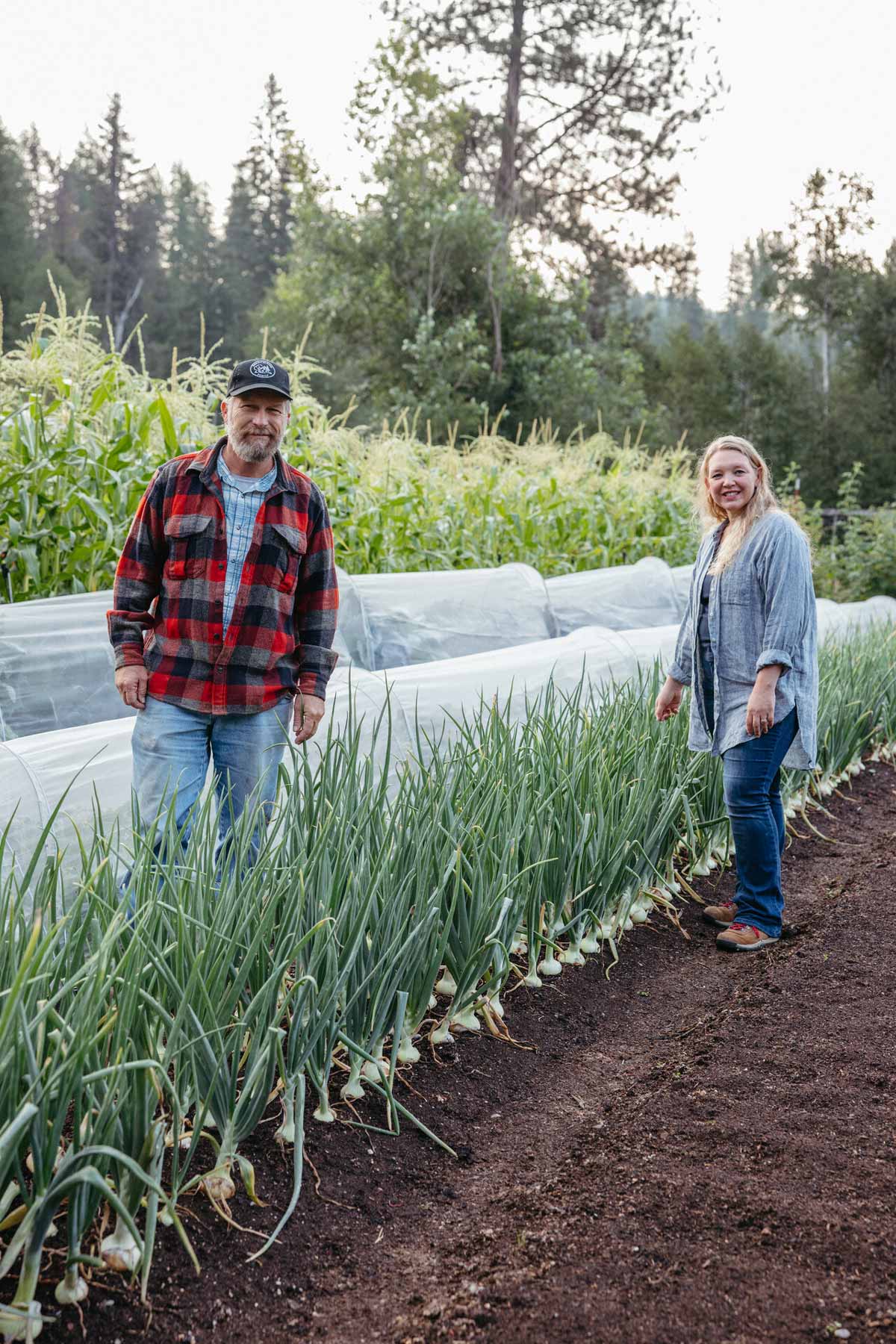 A man and woman standing next to a row of onions in the garden.