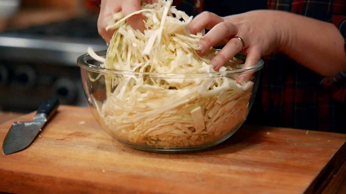 Cabbage and salt being mixed with hands.
