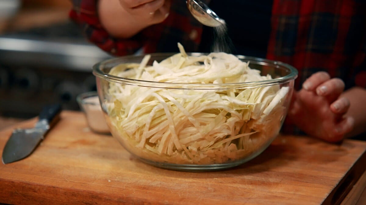 Adding salt to a bowl of cabbage for sauerkraut.