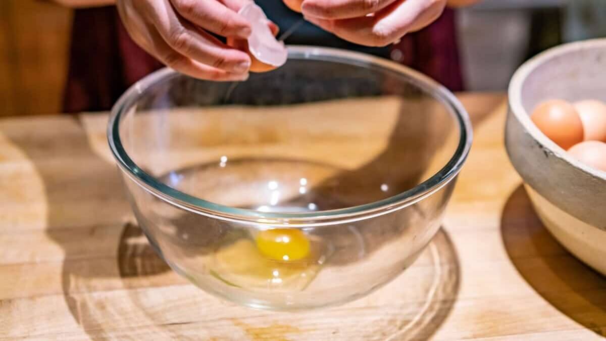 Eggs being cracked into a clear glass bowl.