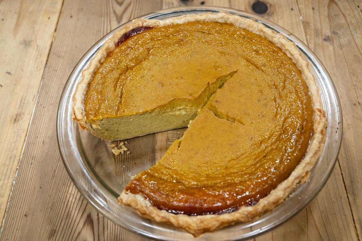A pumpkin pie with a piece cut out of it.