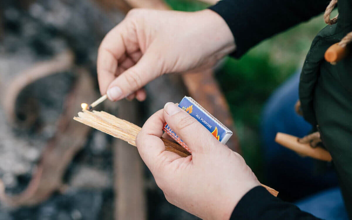 Hands lighting a match for a campfire.