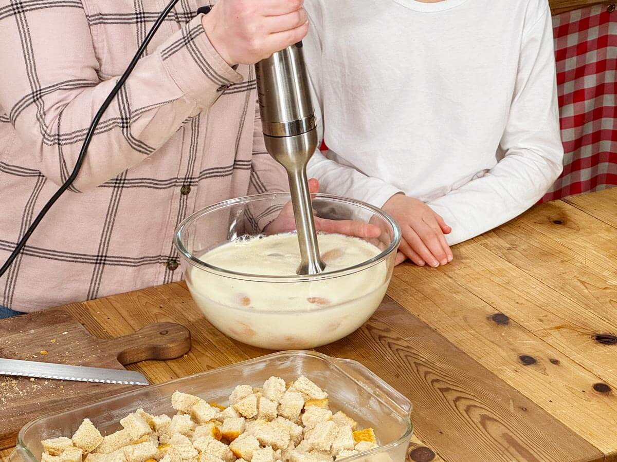 Two young girls blending ingredients with an immersion blender.