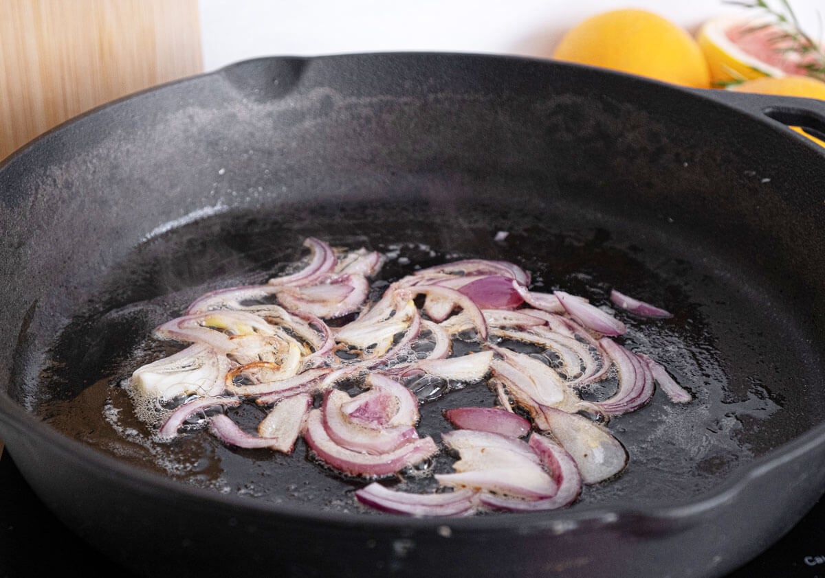 Sliced red onions caramelizing in a cast iron pan.