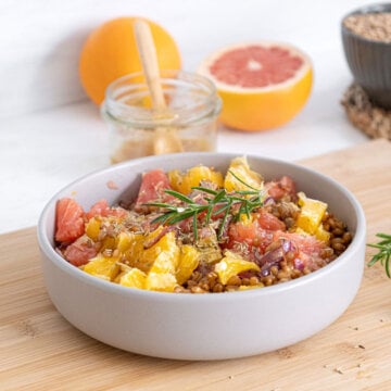 Warm citrus salad served in a white bowl and garnished with a sprig of fresh rosemary.