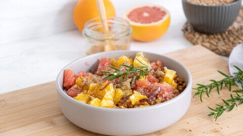 Warm citrus salad served in a white bowl and garnished with a sprig of fresh rosemary.