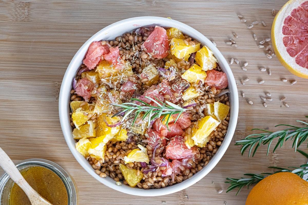 Warm citrus salad served in a white bowl and garnished with a sprig of fresh rosemary.