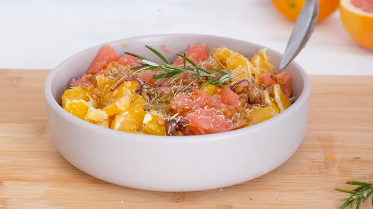 A spoon mixing citrus salad in a white bowl.