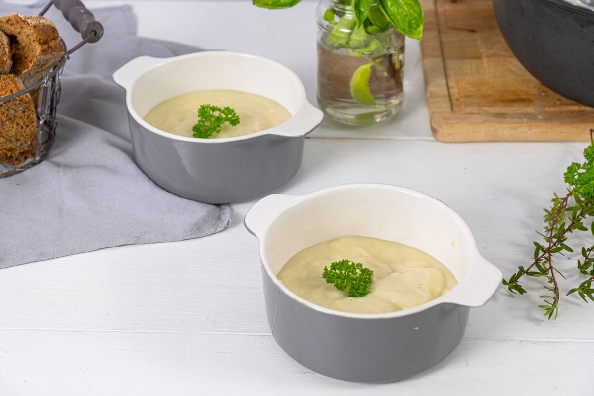 Two bowls filled with cream of chicken soup and garnished with fresh herbs.