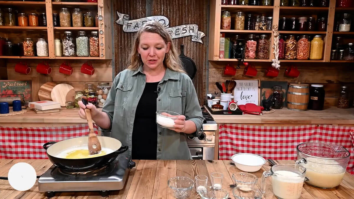 A woman adding flour to melted butter in a saucepan to make a roux.