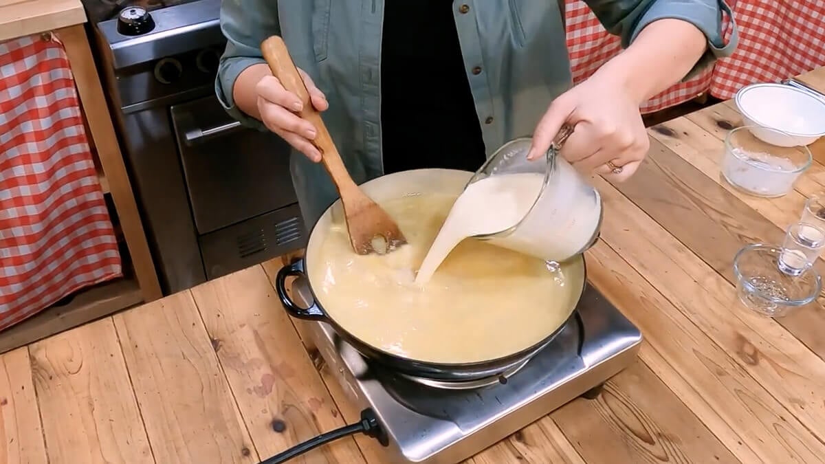 One hand pouring cream into soup while the other hand stirs.