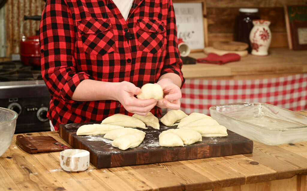 A young woman forming dough into dinner rolls.