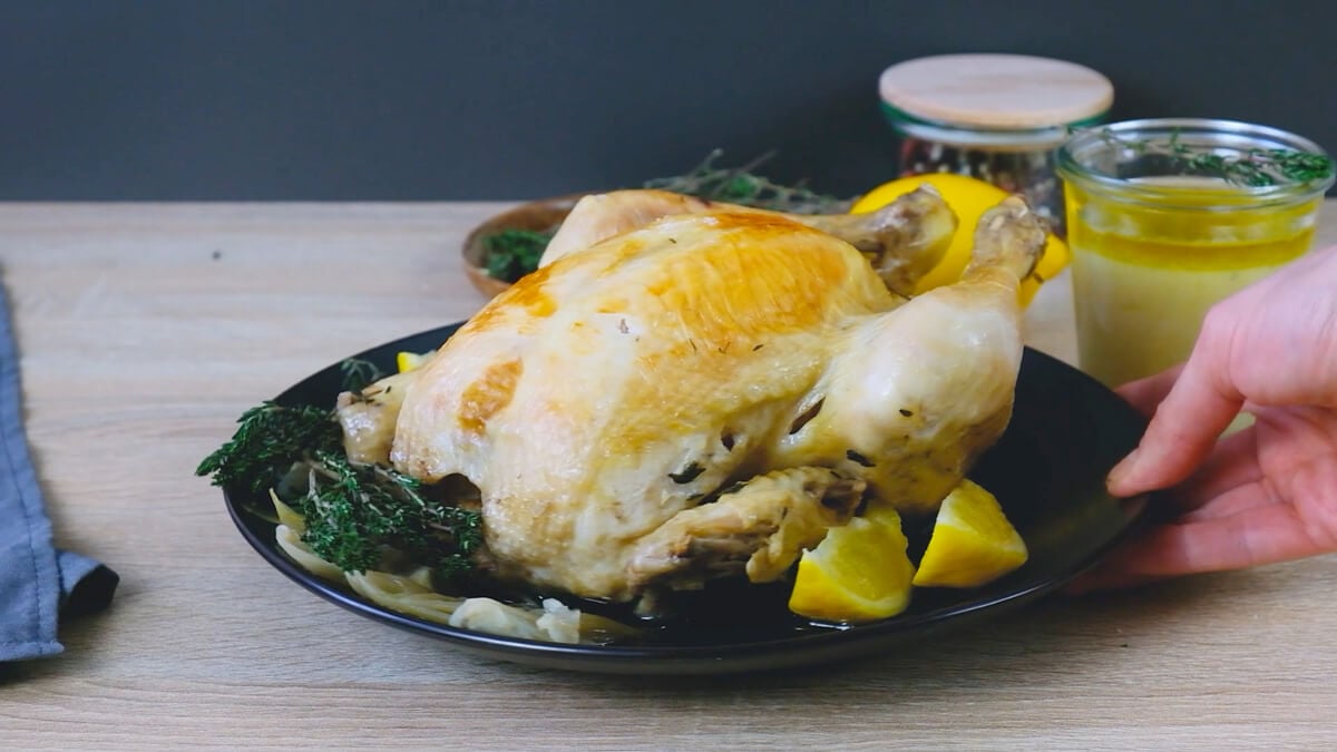 A whole roasted chicken on a platter with onions and preserved lemons.