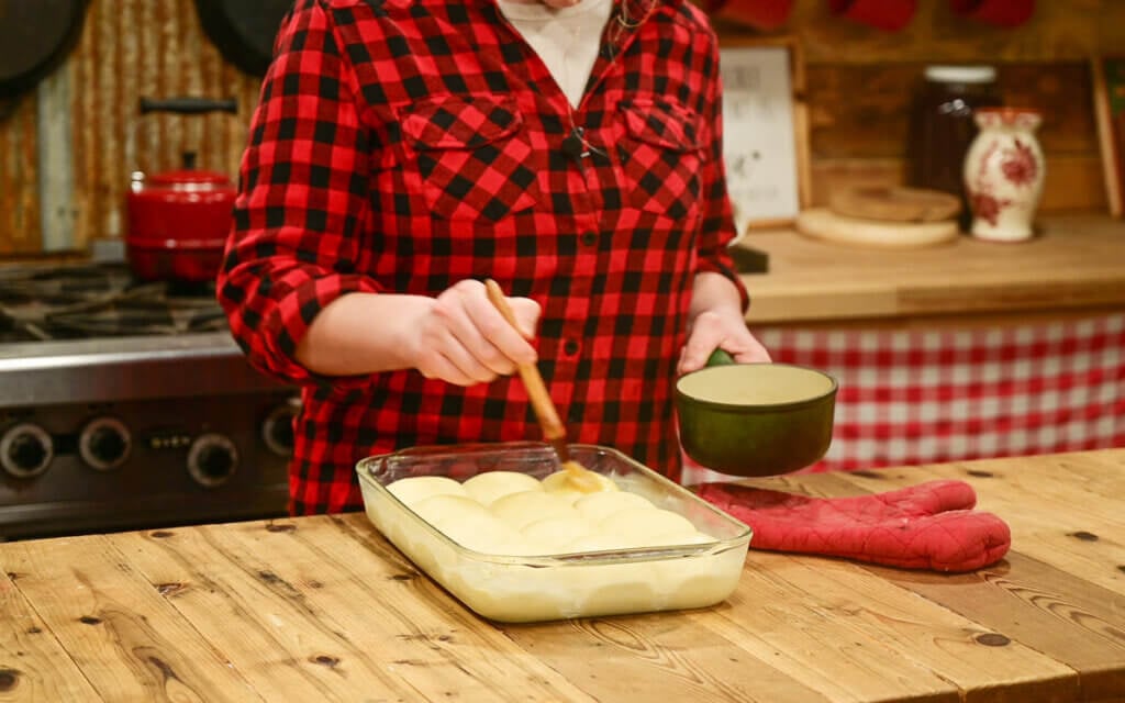 A young girl brushing uncooked dinner rolls with melted butter.