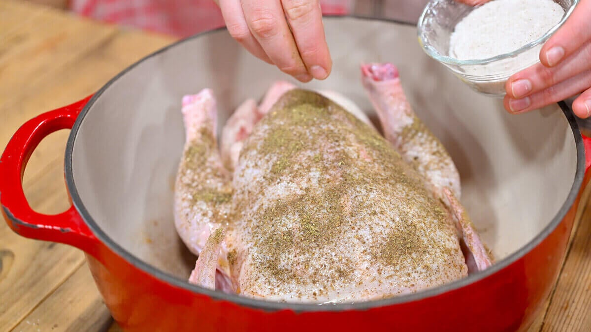 A whole chicken being seasoned with salt.