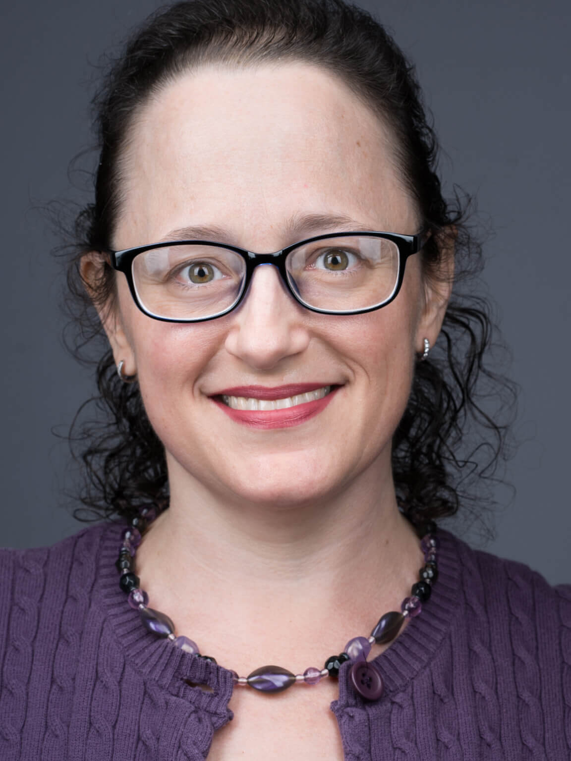 Headshot of a woman in a purple shirt and glasses.