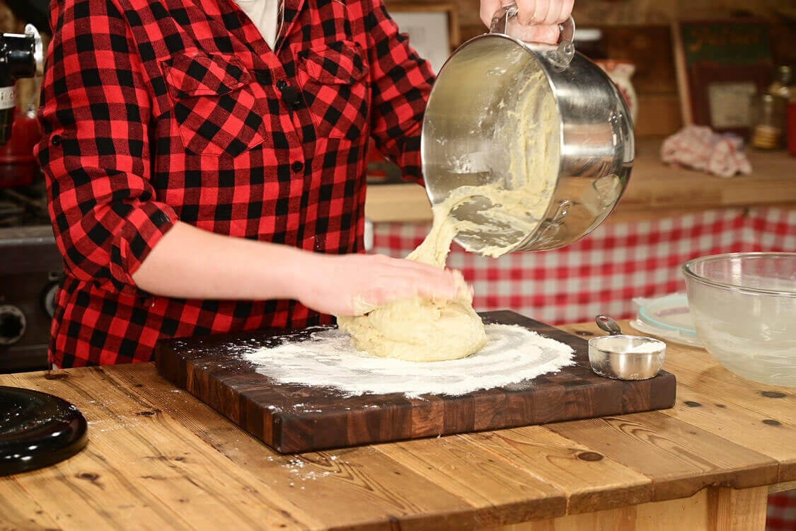 Sourdough dinner roll dough being dumped onto a floured surface.