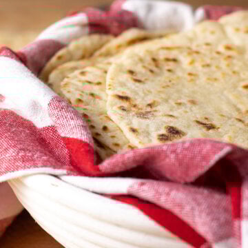 Sourdough discard tortillas stacked in a basked lined with a red and white checkered tea towel.
