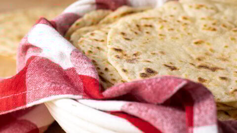 Sourdough discard tortillas stacked in a basked lined with a red and white checkered tea towel.