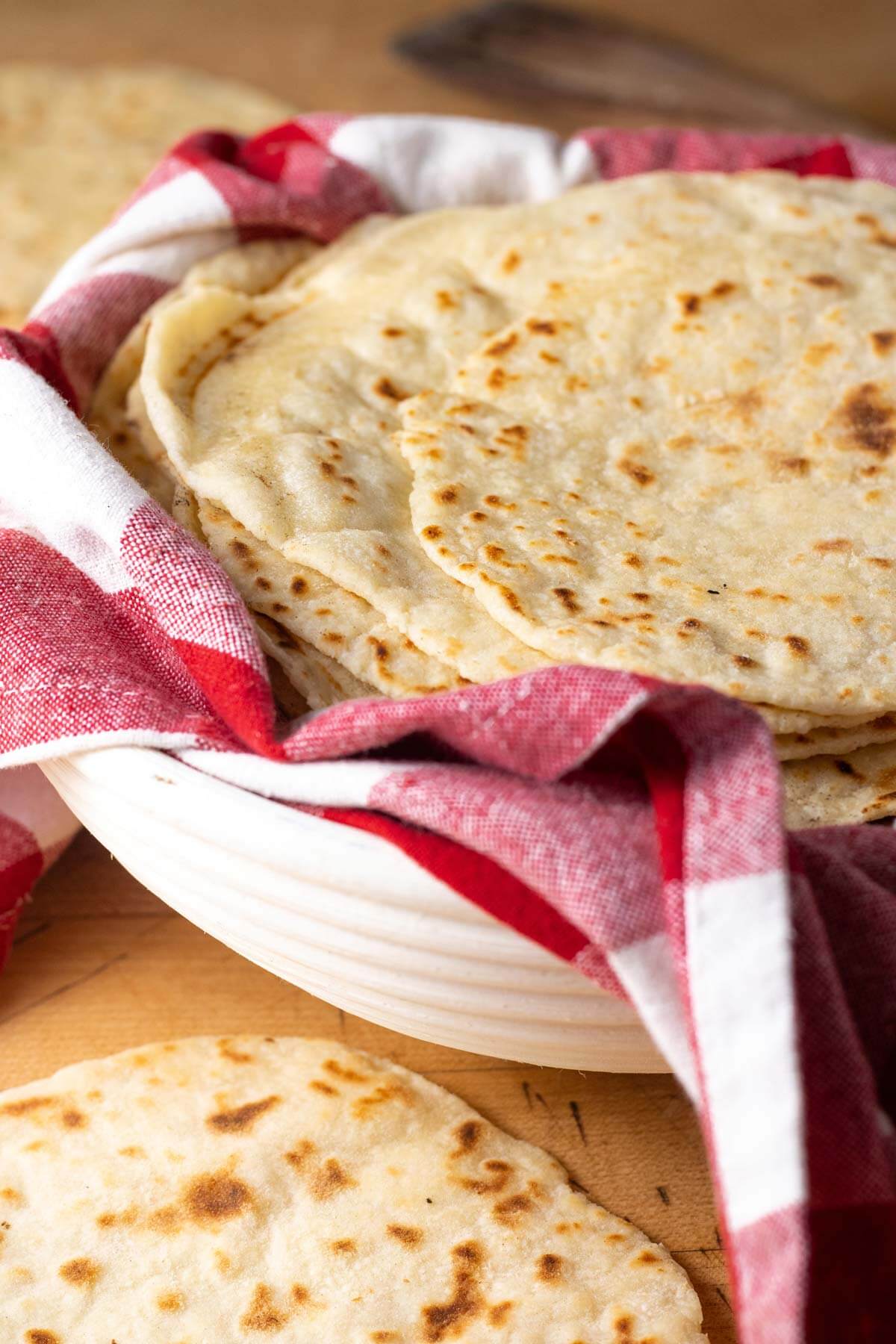 Sourdough discard tortillas stacked in a basked lined with a red and white checkered tea towel.
