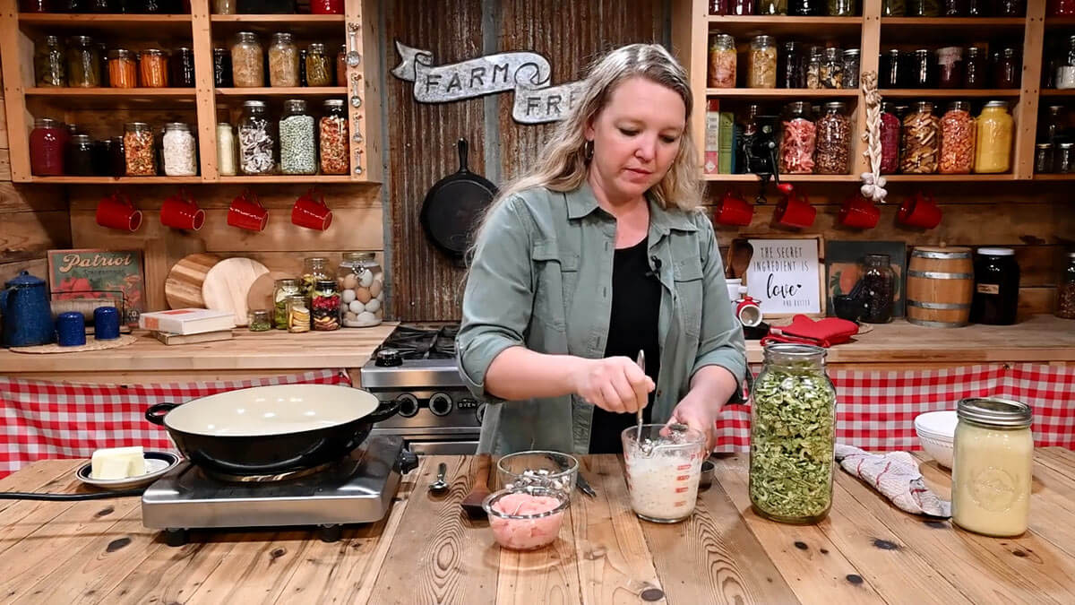 A woman stirring together dry soup mix and chicken broth in a measuring cup.