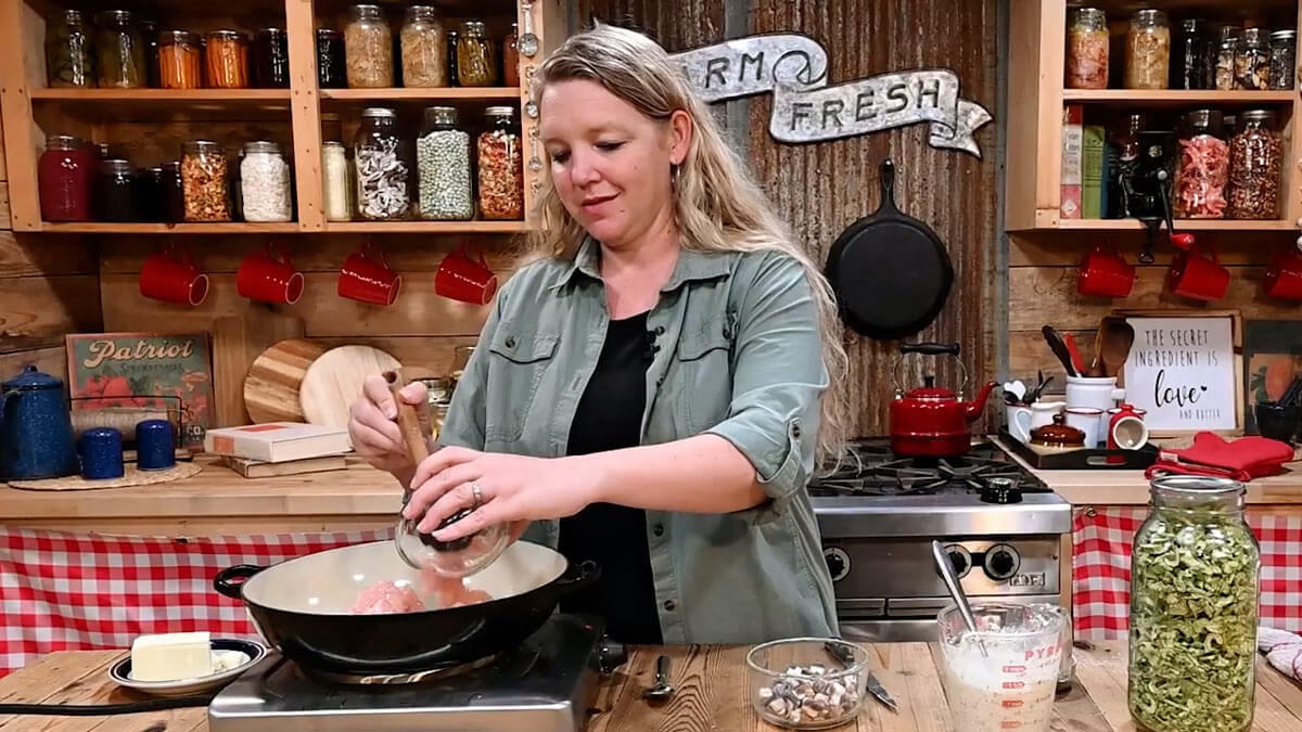 A woman adding chicken to a hot skillet.