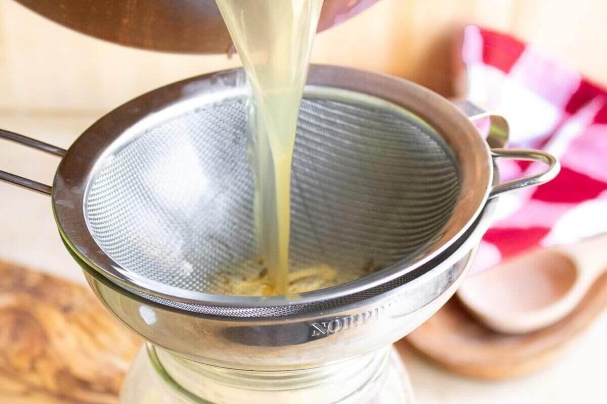 Pouring chicken bone broth through a funnel into a Mason jar.