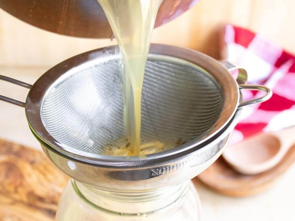 Pouring chicken bone broth through a funnel into a Mason jar.