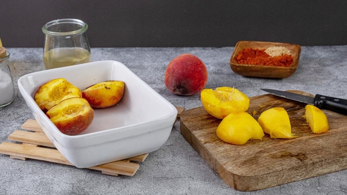 Peaches being sliced in half and placed in a white baking dish.